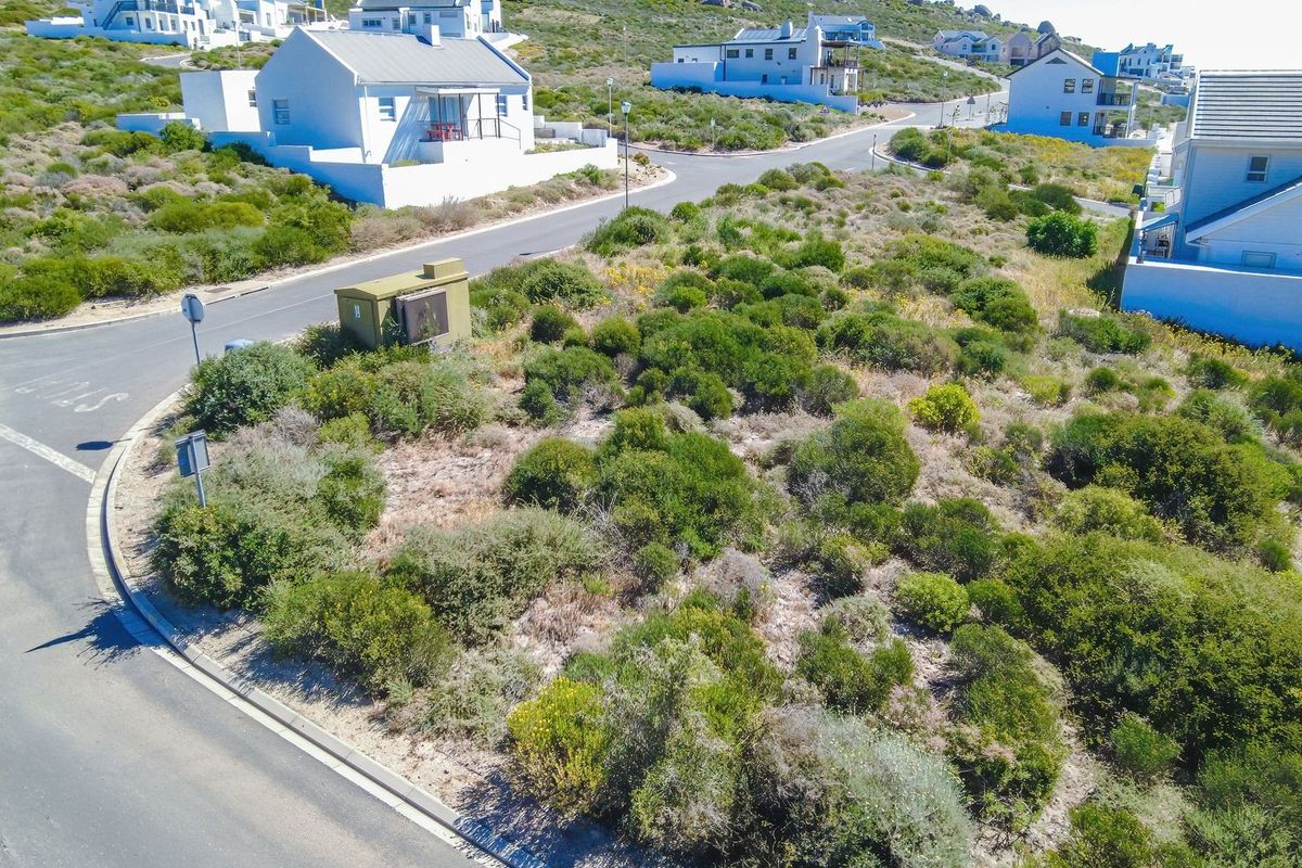 An aerial view of a vacant residential plot situated on a corner lot, featuring native coastal vegetation and adjacent paved street access.