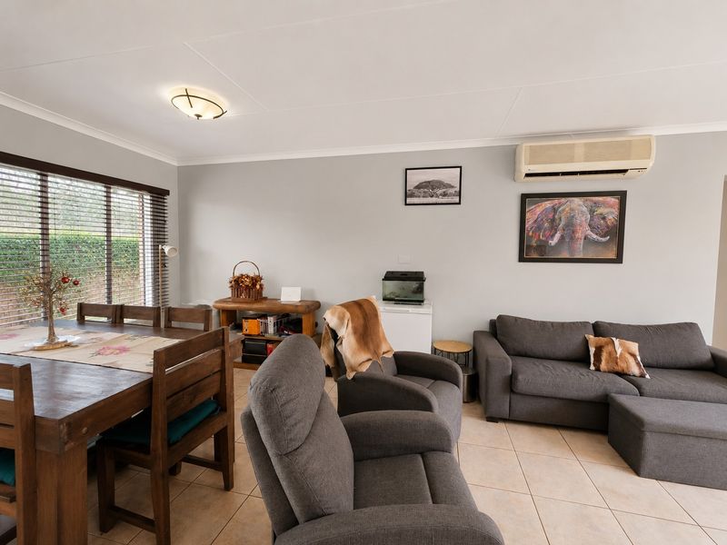 An open-plan living and dining area featuring neutral tiled flooring, a wall-mounted air conditioning unit, and large windows with venetian blinds.