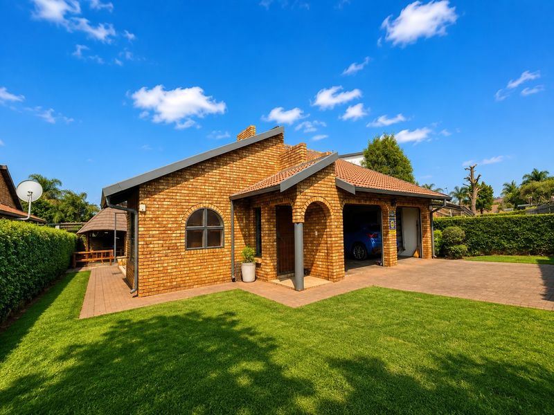A well-maintained face brick house featuring a tiled roof, arched entrance, double garage, paved driveway, and neatly landscaped garden.