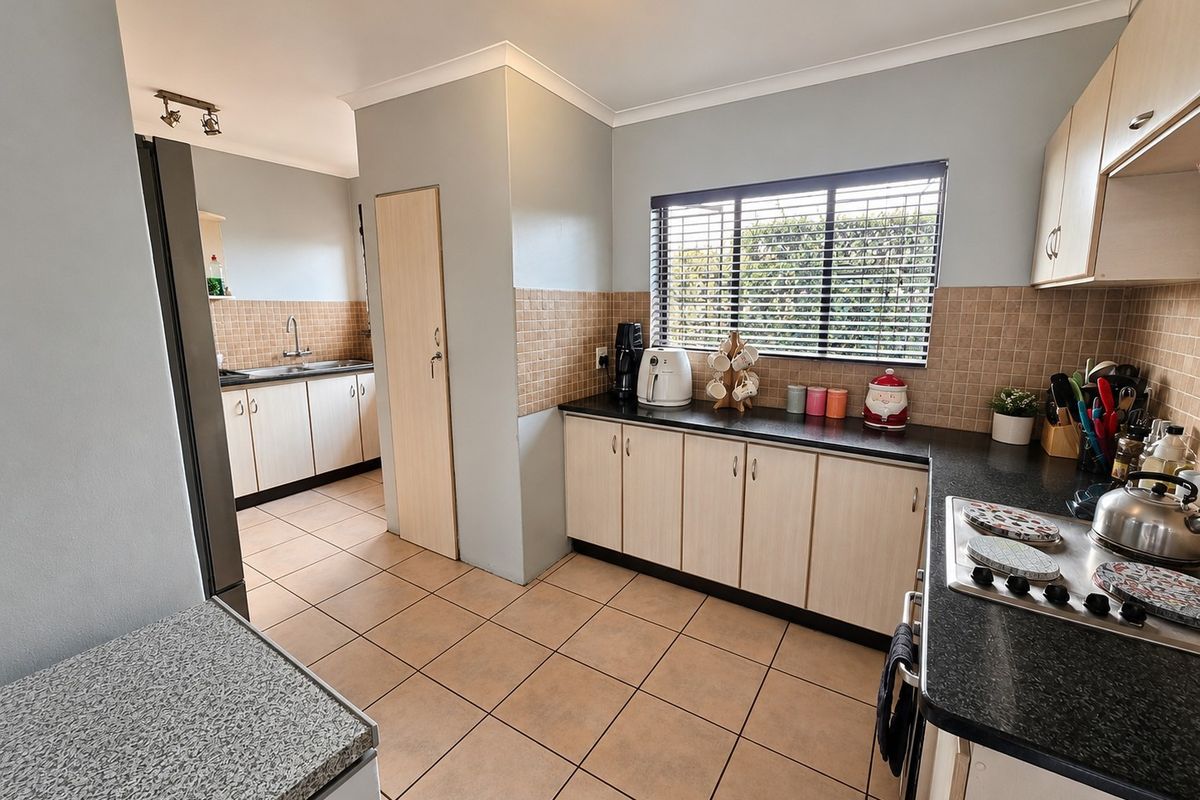 Functional kitchen featuring light wood-finish cabinetry, dark granite countertops, ceramic tile flooring, and a separate scullery area with a double sink.