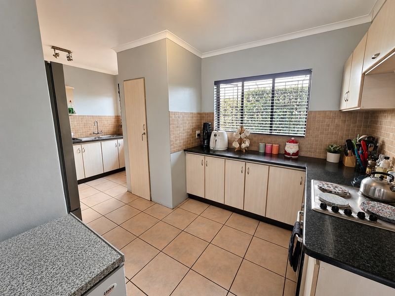 Functional kitchen featuring light wood-finish cabinetry, dark granite countertops, ceramic tile flooring, and a separate scullery area with a double sink.