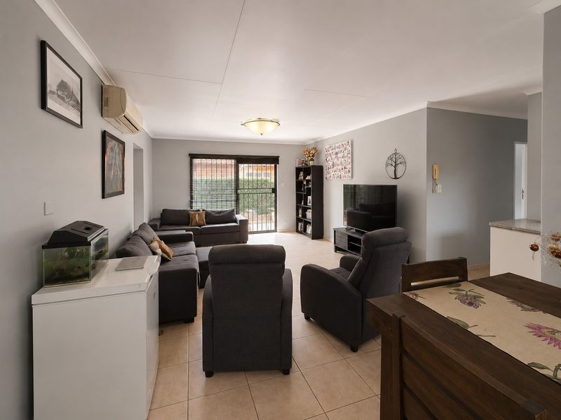 A spacious living room featuring tiled flooring, a split-system air conditioner, and a sliding glass door with security gate leading to the exterior.