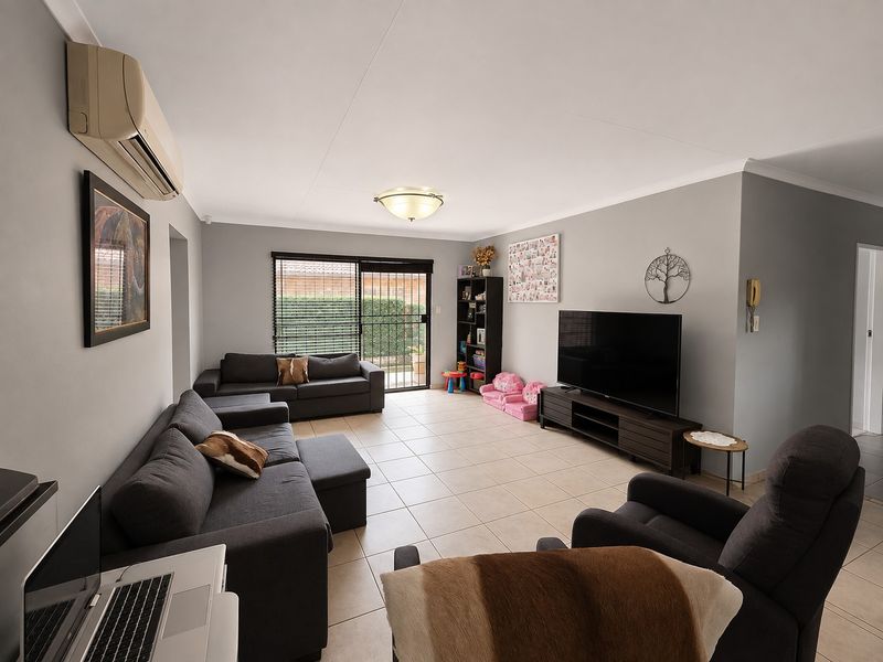 A spacious living room featuring neutral tiled flooring, a wall-mounted split-system air conditioner, and a sliding glass door providing access to the exterior.