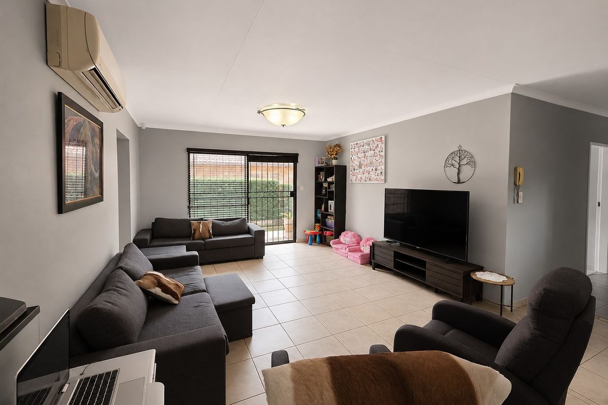 A spacious living room featuring neutral tiled flooring, a wall-mounted split-system air conditioner, and a sliding glass door providing access to the exterior.