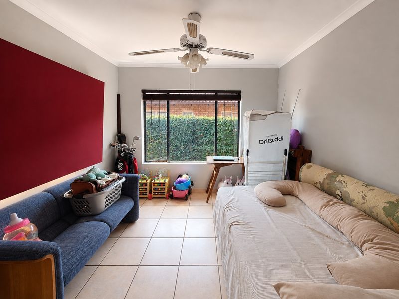 A bedroom featuring tiled flooring, a ceiling fan, and a window with blinds, offering a functional space with neutral wall finishes.