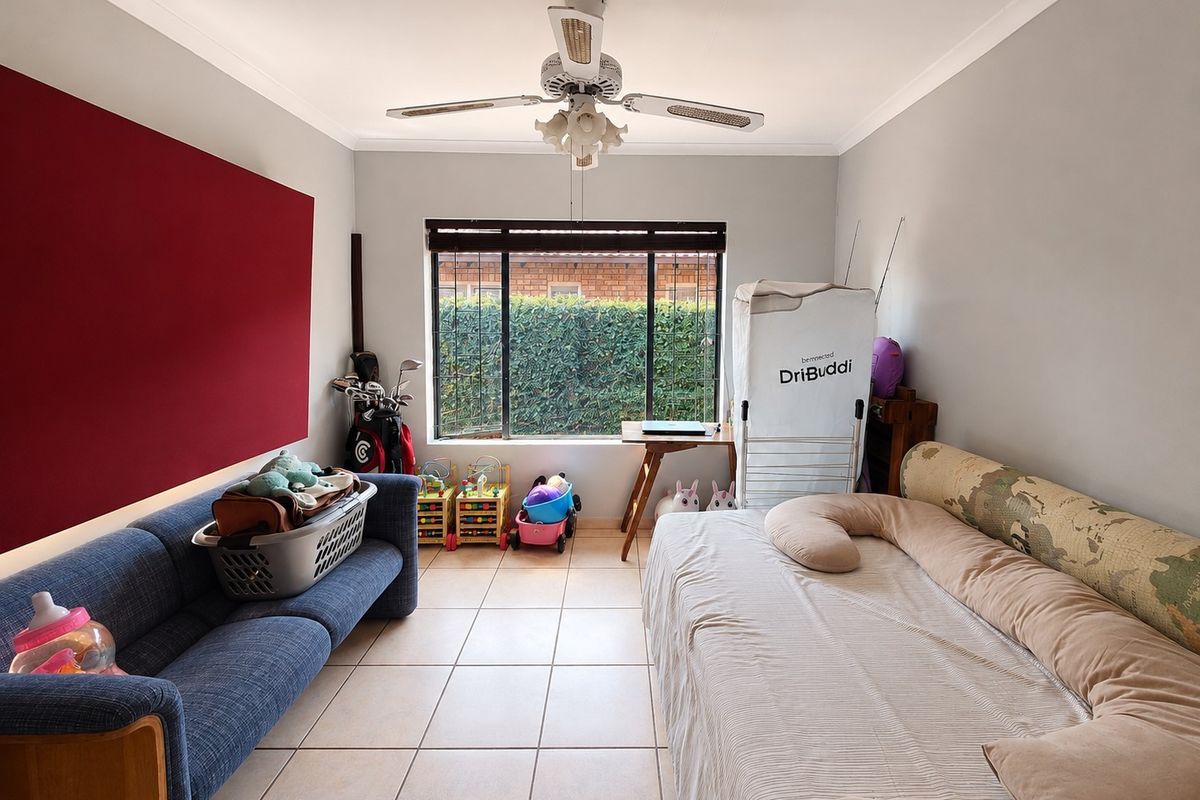 A bedroom featuring tiled flooring, a ceiling fan, and a window with blinds, offering a functional space with neutral wall finishes.