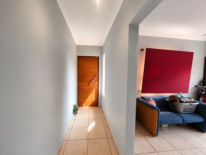 A bright hallway featuring tiled flooring and a modern timber entrance door, leading into an adjacent living area.