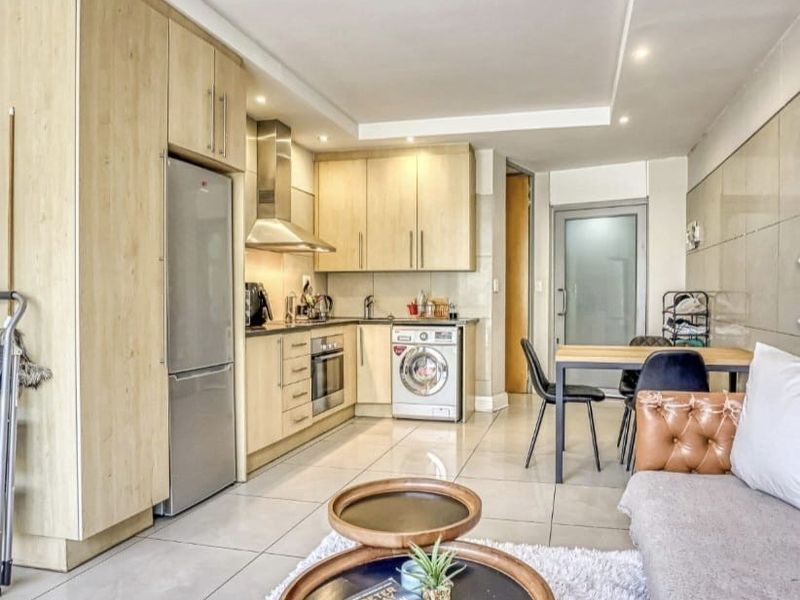 Open-plan living area featuring a modern kitchen with light wood cabinetry, stainless steel appliances, tiled flooring, and recessed lighting.