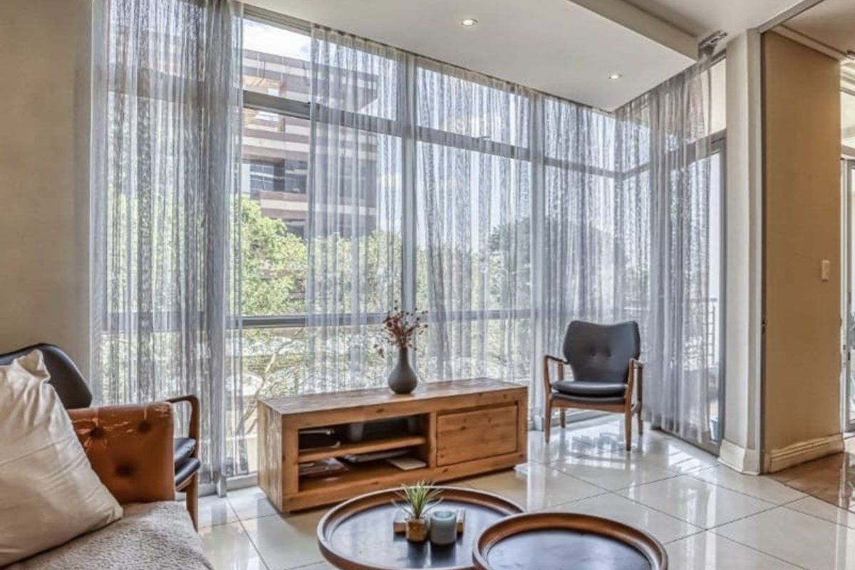 A bright living room featuring large floor-to-ceiling windows, polished tiled flooring, and a modern bulkhead ceiling with recessed lighting.