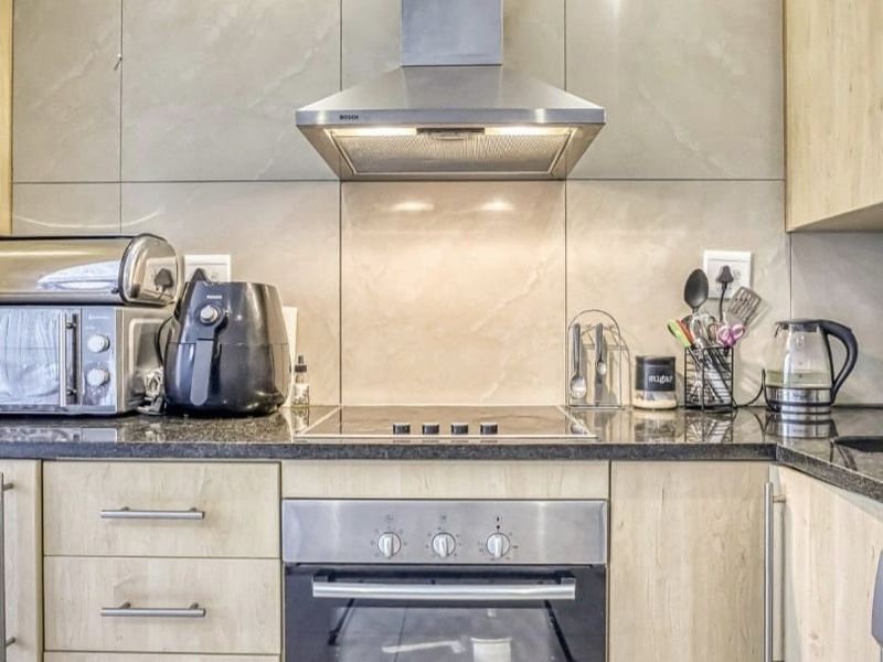 Modern kitchen featuring sleek cabinetry, granite countertops, a built-in oven, electric hob, and a stainless steel extractor fan.