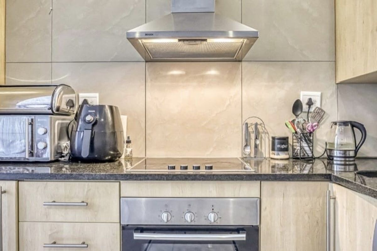 Modern kitchen featuring sleek cabinetry, granite countertops, a built-in oven, electric hob, and a stainless steel extractor fan.