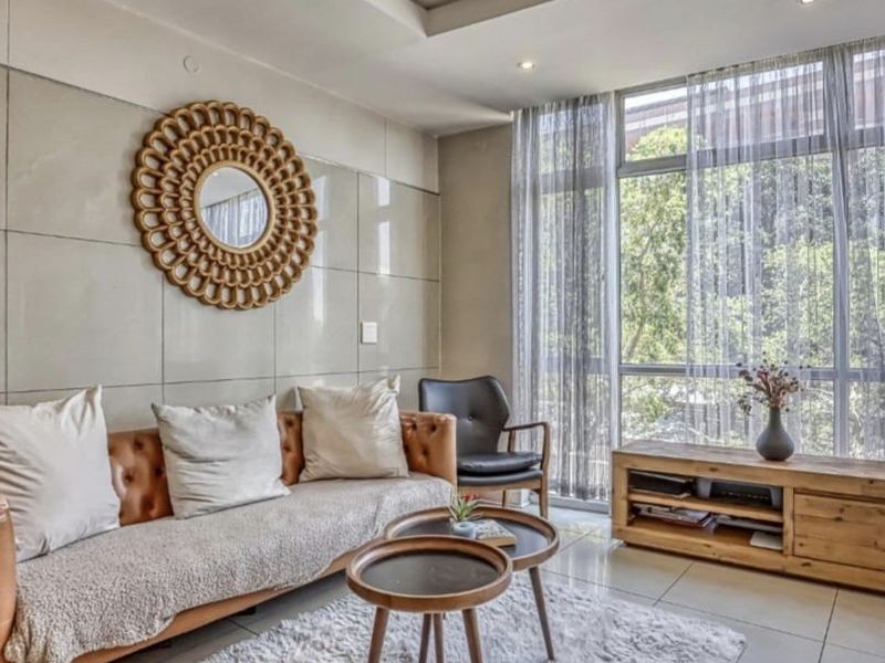 A bright and modern living room featuring large floor-to-ceiling windows, tiled flooring, and a contemporary tiled feature wall with recessed ceiling lighting.