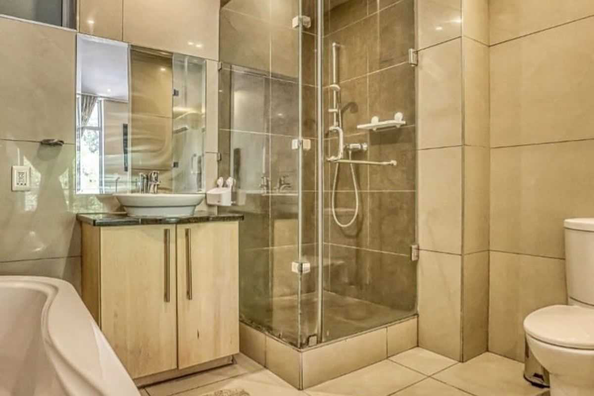Modern bathroom featuring a glass-enclosed shower, vessel sink with vanity cabinet, bathtub, and neutral floor-to-ceiling tiling.