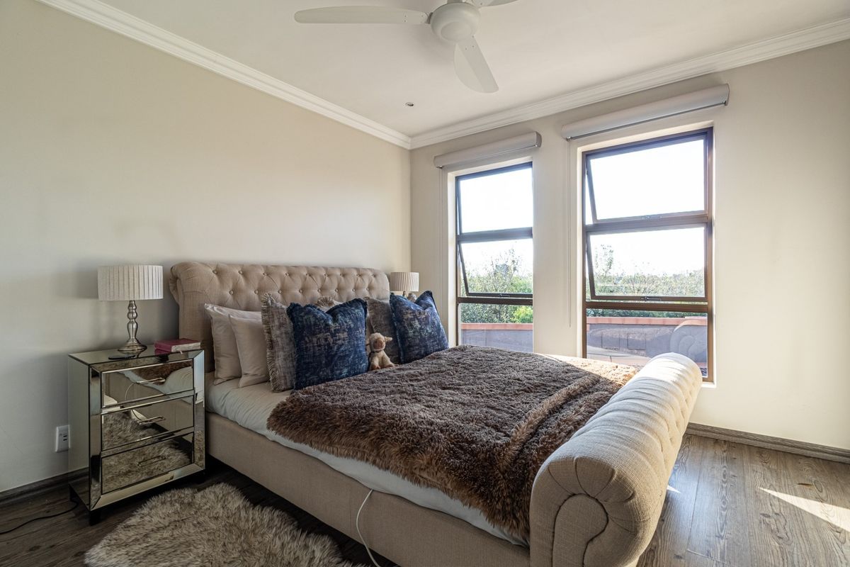 A well-maintained bedroom featuring laminate flooring, modern aluminium window frames, and a ceiling fan, offering a bright and comfortable living space.