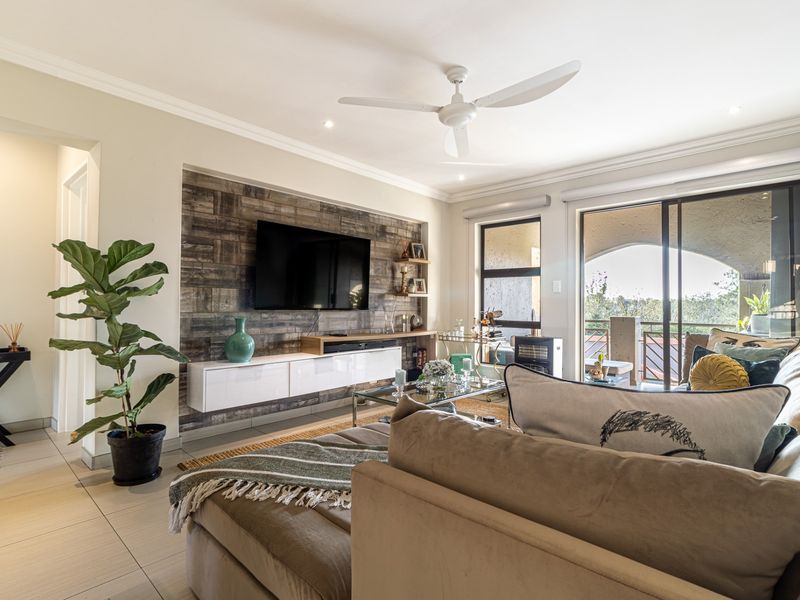 A well-maintained living room featuring a wood-look accent wall, built-in media cabinetry, tiled floors, and sliding glass doors leading to a balcony.