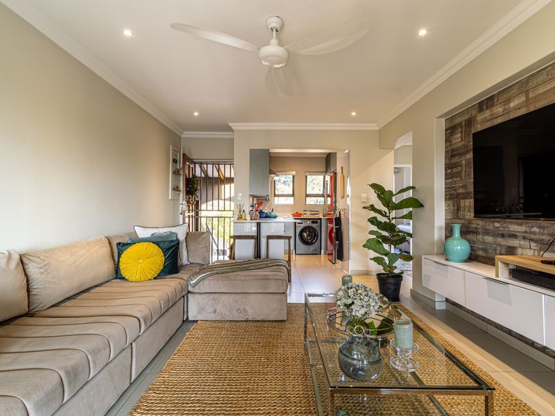 An open-plan living area featuring tiled floors, recessed lighting, and a modern media wall, seamlessly connecting to a functional kitchen space.