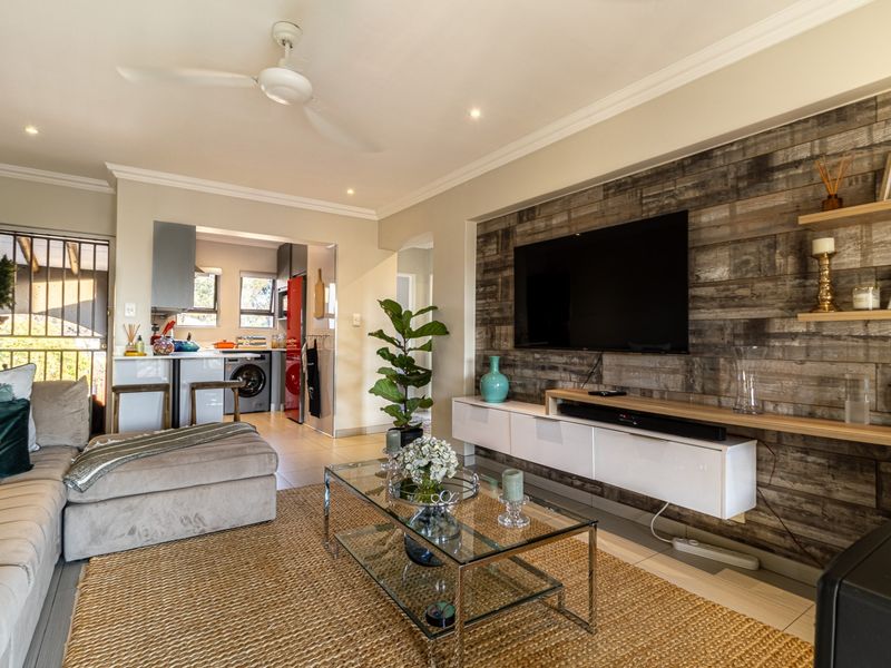An open-plan living area featuring a wood-accented media wall, built-in cabinetry, recessed lighting, and a ceiling fan, seamlessly connecting to the kitchen space.