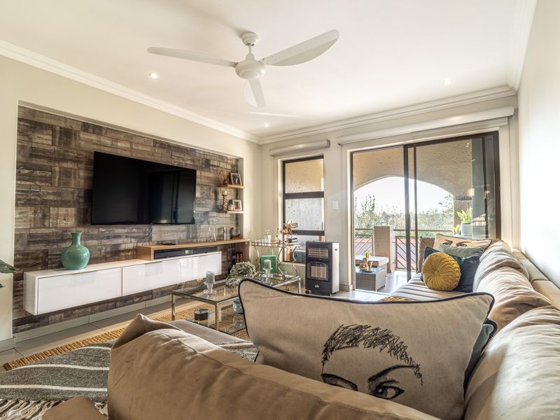A well-lit living room featuring a wood-look feature wall, floating cabinetry, ceiling fan, and sliding glass doors leading to an outdoor balcony area.