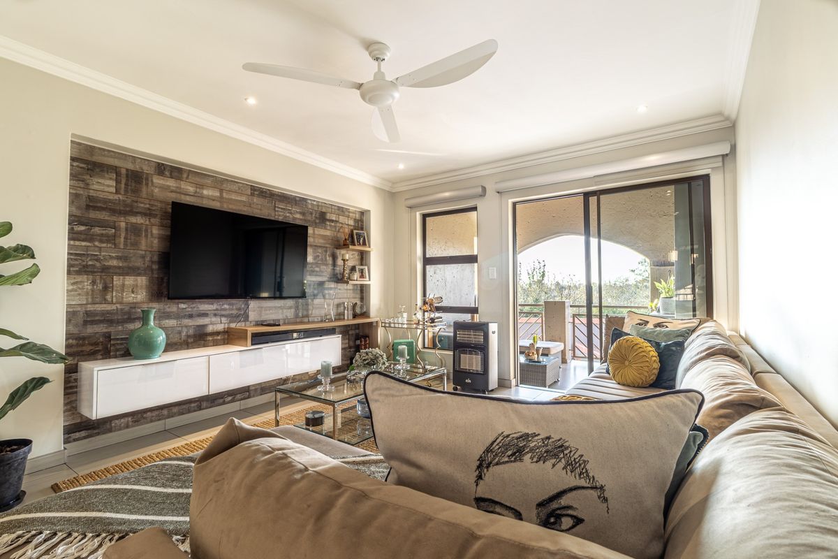 A well-lit living room featuring a wood-look feature wall, floating cabinetry, ceiling fan, and sliding glass doors leading to an outdoor balcony area.