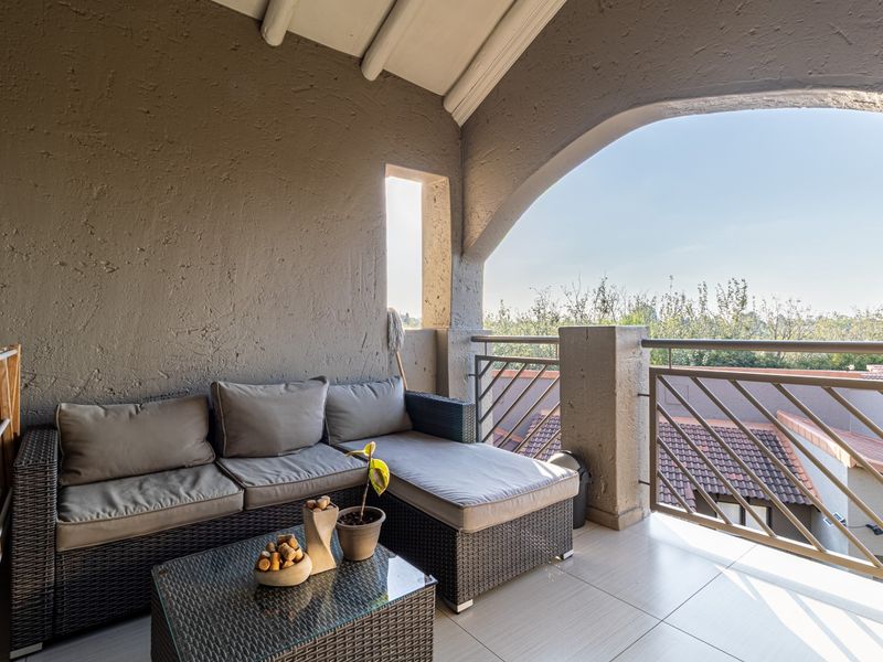 A covered balcony featuring tiled flooring, an arched architectural opening, and a metal balustrade, offering an open-air space with views of the surrounding area.