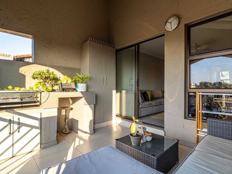 A covered balcony featuring a built-in braai, tiled flooring, and direct access to the living area through sliding glass doors.