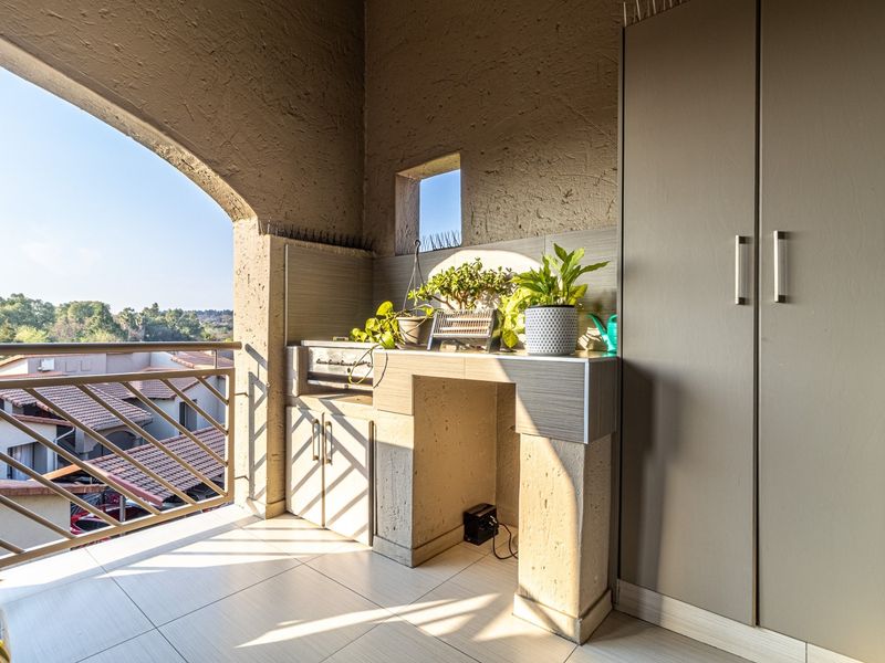 A covered balcony featuring a built-in braai, tiled flooring, and a large storage cupboard, offering an elevated view of the surrounding neighborhood.