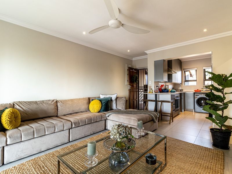 Open-plan living area featuring a modern kitchen with built-in appliances, breakfast bar, tiled flooring, and a ceiling fan, creating a cohesive and functional space.