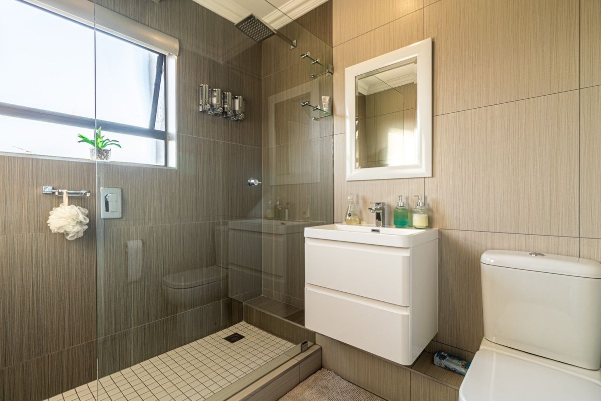 Modern bathroom featuring a walk-in shower with a rain shower head, wall-mounted vanity, and neutral tiled finishes throughout.