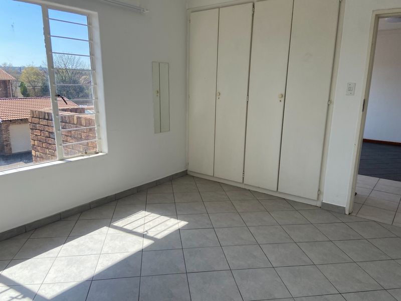 An empty bedroom featuring tiled flooring, built-in cupboards, and a window with security bars, offering a blank canvas for personalization.