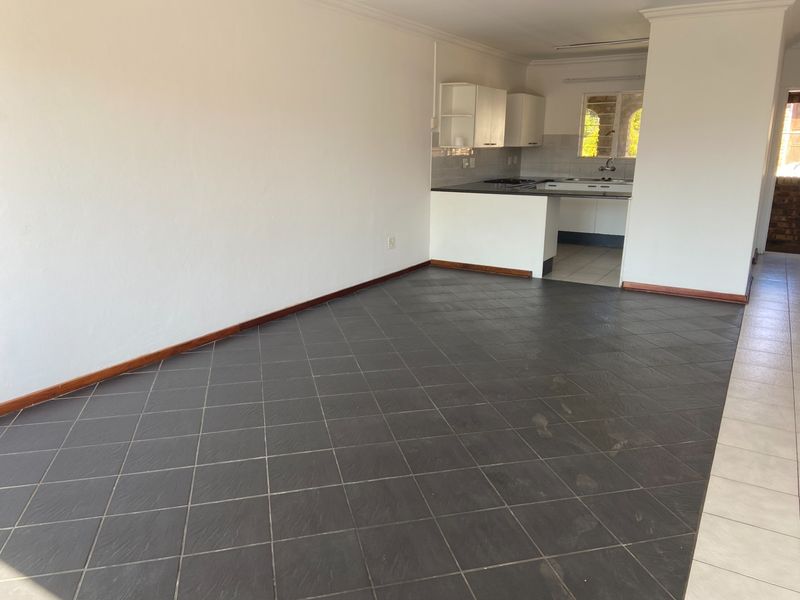 An empty open-plan living and kitchen area featuring dark tiled flooring, built-in cabinetry, and neutral walls, offering a blank canvas for potential updates.
