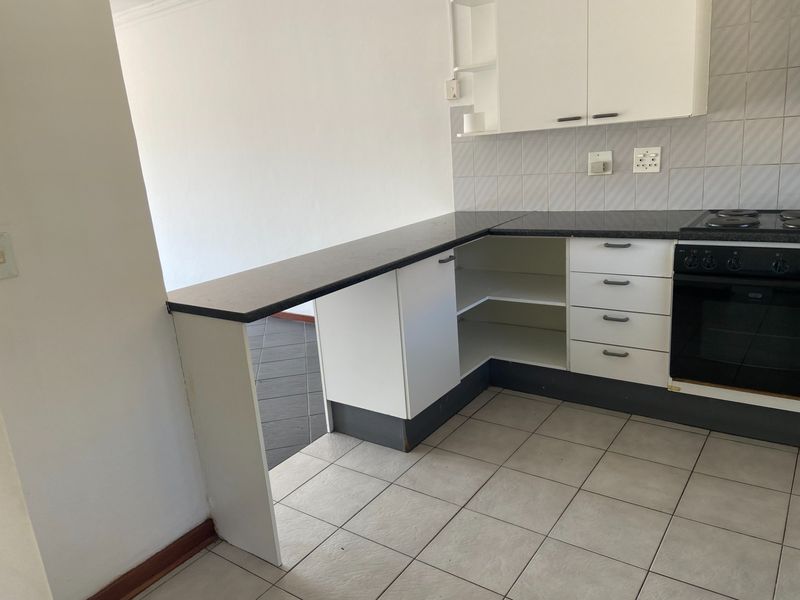 A compact kitchen featuring white cabinetry, a dark laminate countertop with an integrated breakfast bar, built-in oven, and tiled flooring.