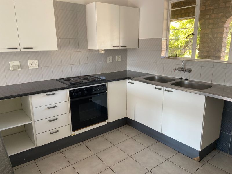 A functional kitchen featuring white cabinetry, dark laminate countertops, a built-in oven and hob, and a double stainless steel sink with tiled backsplash.