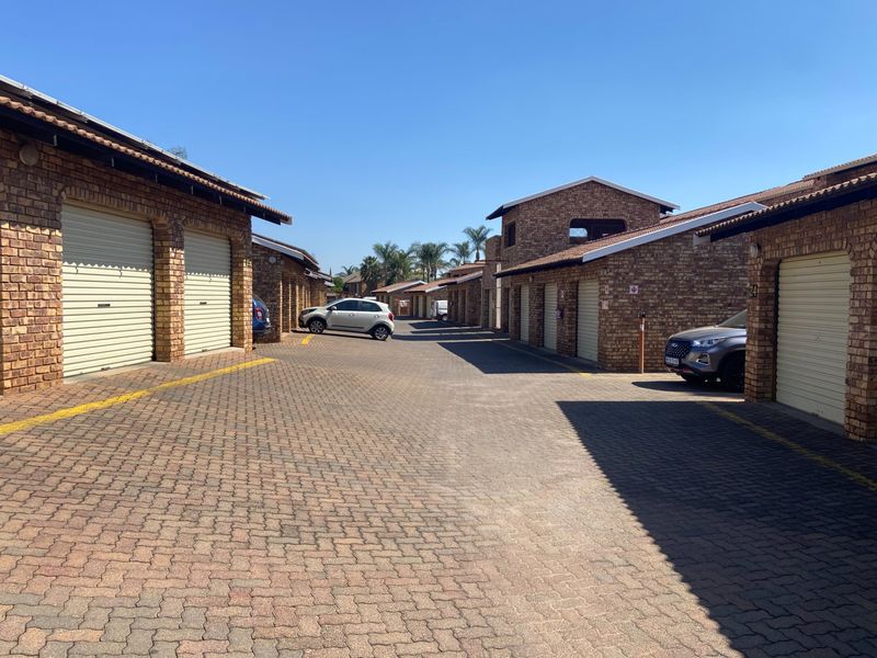 A view of a residential complex driveway featuring multiple face brick garage units with roller shutter doors and paved access.
