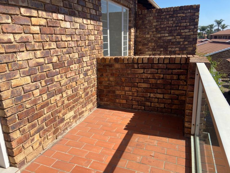 A private balcony featuring face brick walls, terracotta tile flooring, and a modern glass balustrade with a metal handrail.