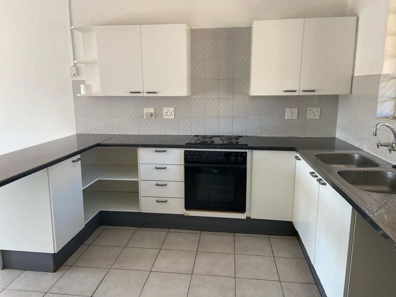 A functional kitchen featuring white cabinetry, dark countertops, a built-in oven and hob, and tiled finishes throughout.