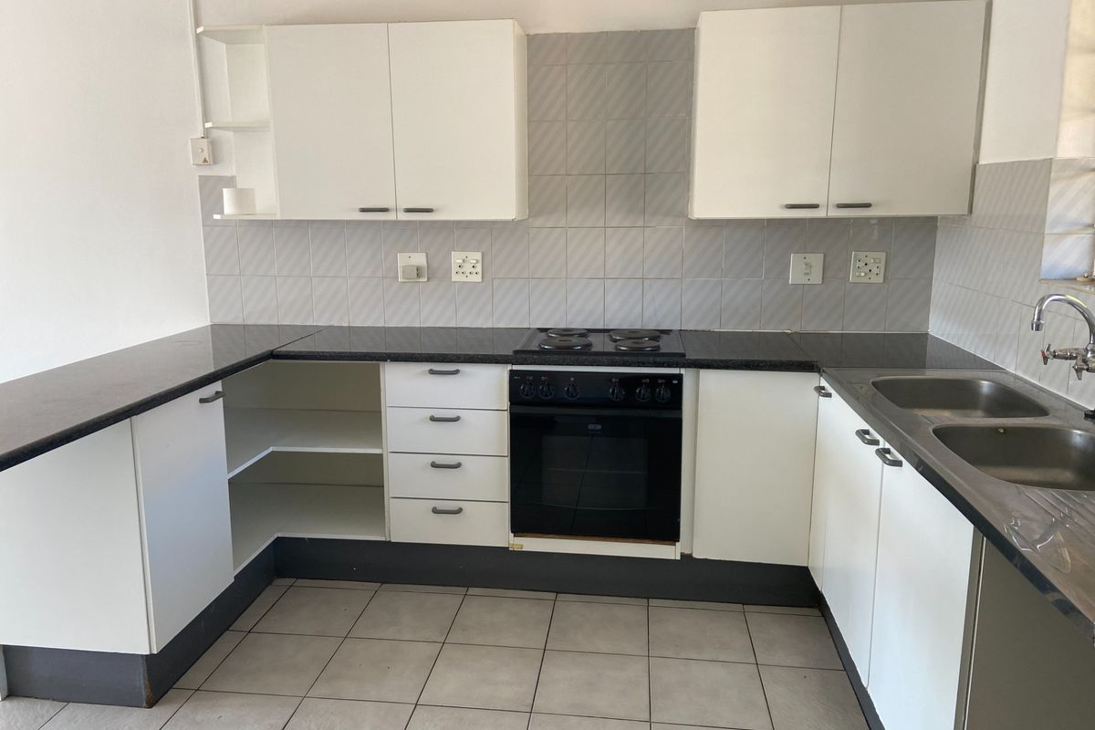 A functional kitchen featuring white cabinetry, dark countertops, a built-in oven and hob, and tiled finishes throughout.