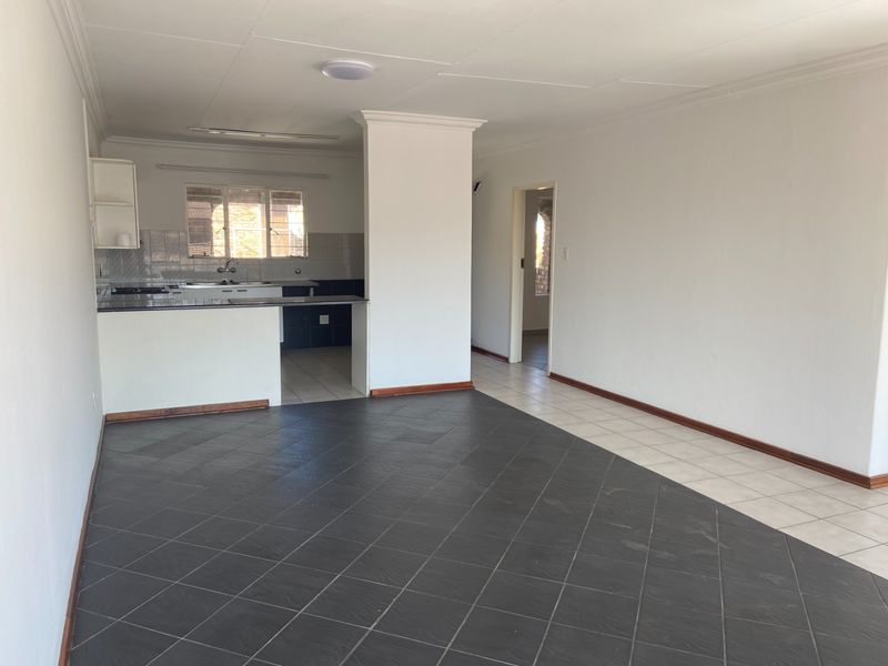 An open-plan living and kitchen area featuring tiled flooring, neutral walls, and a functional kitchen layout with built-in cabinetry and counter space.