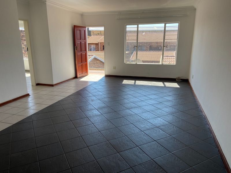 A bright, empty living area featuring dark tiled flooring, neutral walls, and direct access to an outdoor space through a timber door.