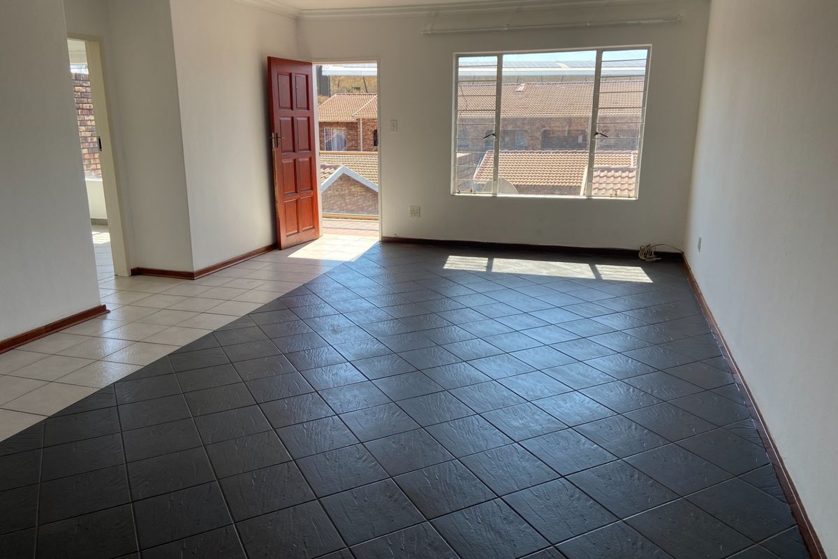 A bright, empty living area featuring dark tiled flooring, neutral walls, and direct access to an outdoor space through a timber door.