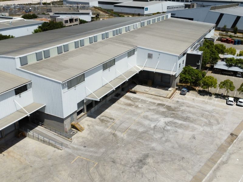 Aerial view of a large industrial warehouse facility featuring extensive concrete yard space, multiple loading docks, and covered parking areas.