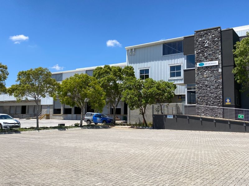 Front view of a modern industrial facility featuring a paved parking area, loading bays, and a combination of metal and stone exterior finishes.