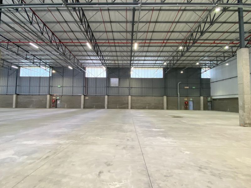 A spacious, open-plan industrial warehouse featuring high ceilings, exposed steel trusses, concrete flooring, and integrated fire sprinkler systems.