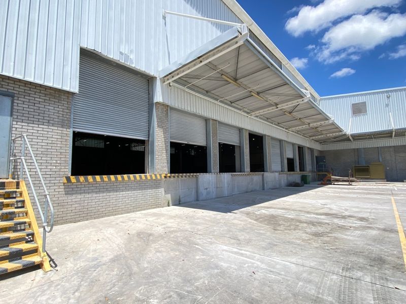 Industrial warehouse exterior featuring multiple roller shutter loading bays, a concrete loading dock, and a protective canopy over the service area.