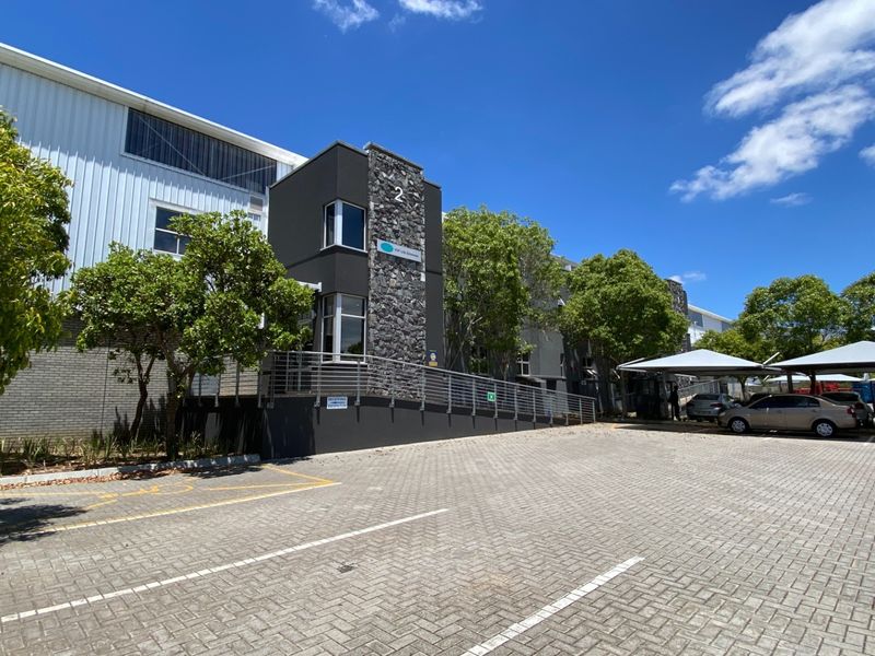Front exterior view of an industrial property featuring a paved parking area, stone-clad entrance facade, and metal shade structures.