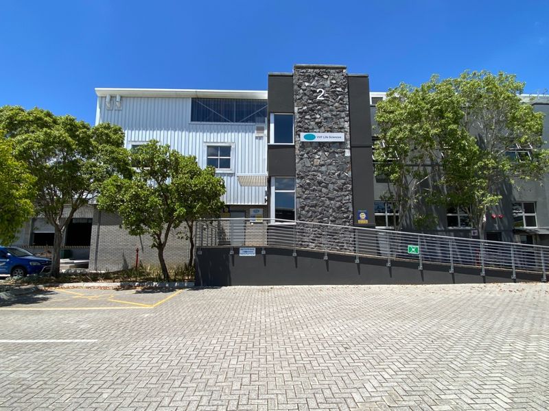 Front exterior view of a modern industrial building featuring stone and metal cladding, a paved parking area, and an accessible ramp entrance.