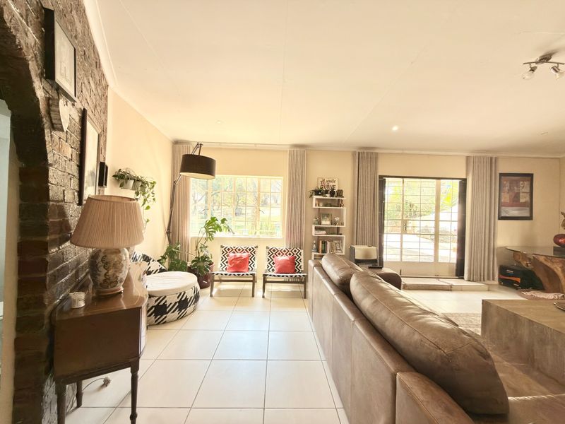 Spacious living room featuring an exposed brick feature wall, neutral tiled flooring, and large windows providing natural light with access to the exterior.