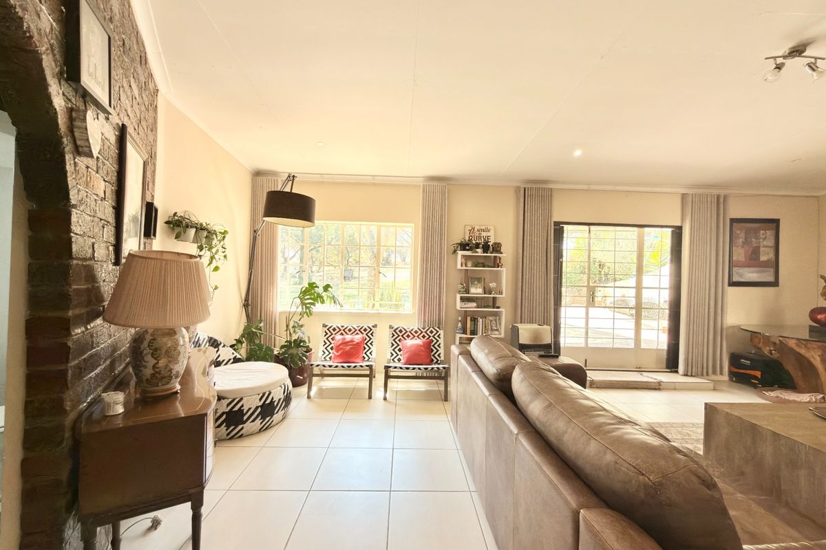 Spacious living room featuring an exposed brick feature wall, neutral tiled flooring, and large windows providing natural light with access to the exterior.