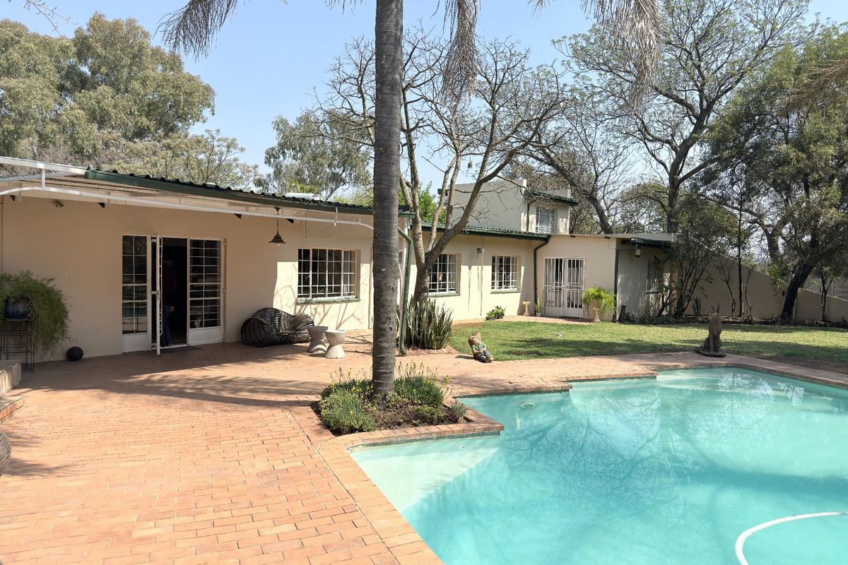 Rear view of the house featuring a swimming pool, brick paved patio area, and established garden surroundings.