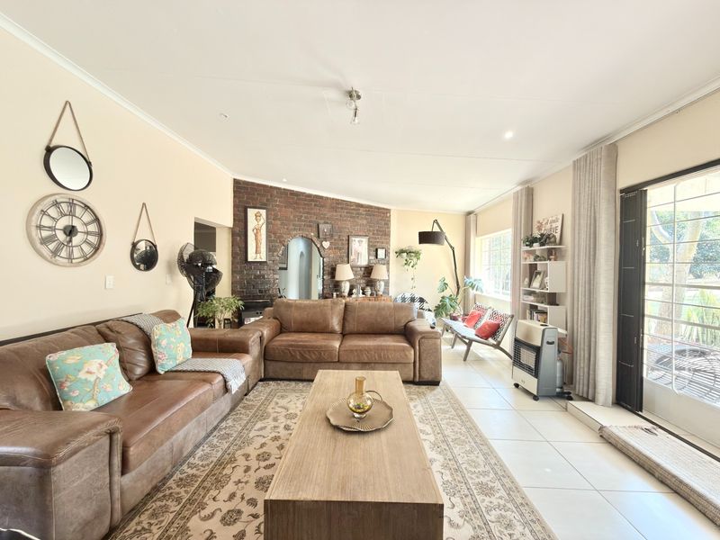 Spacious living room featuring an exposed brick accent wall, neutral tiled flooring, and large sliding glass doors providing natural light and garden access.
