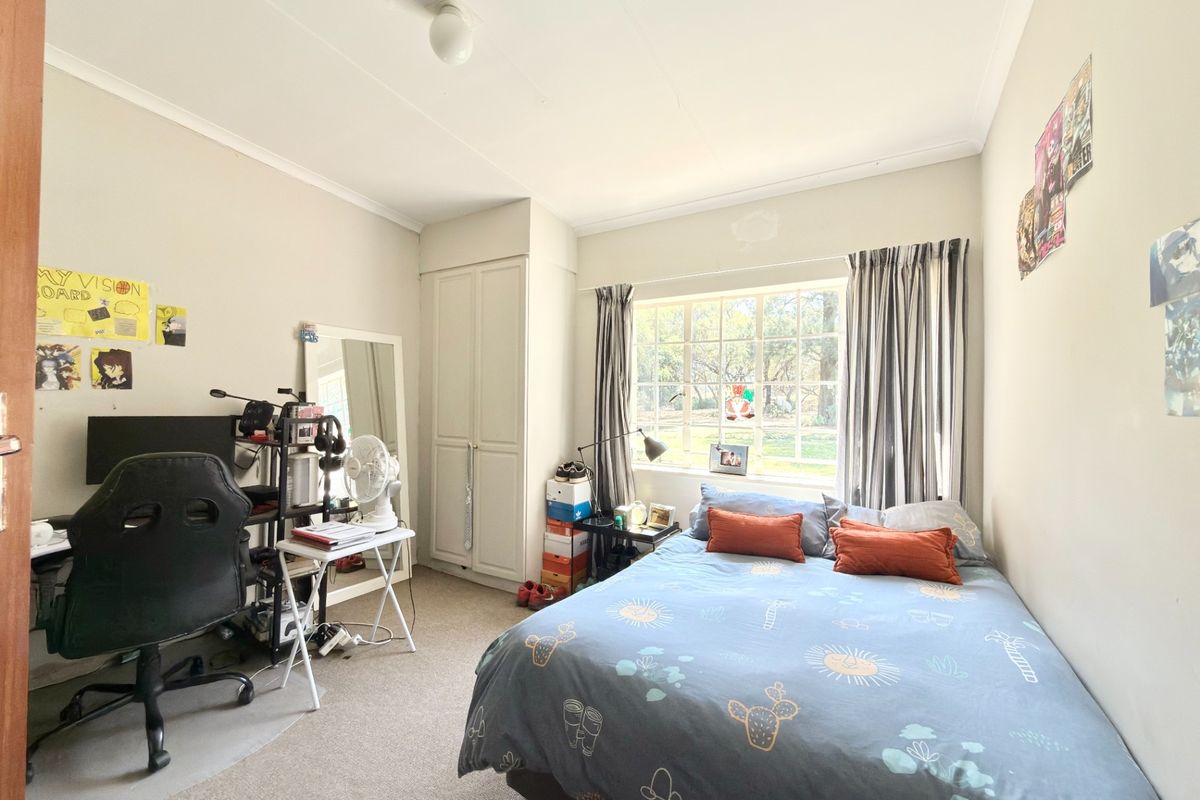A functional bedroom featuring a built-in wardrobe, carpeted flooring, and a large window providing natural light.